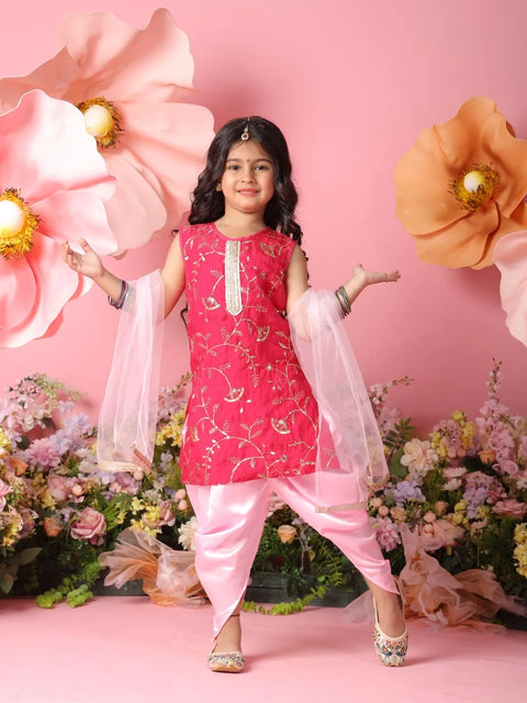 Young girl in a pink traditional outfit standing against a pink floral backdrop