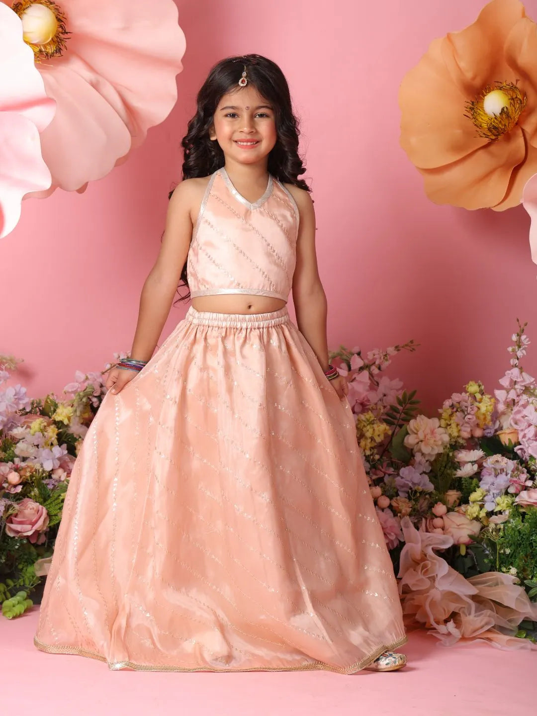 Young girl in a pink traditional outfit standing against a pink floral background
