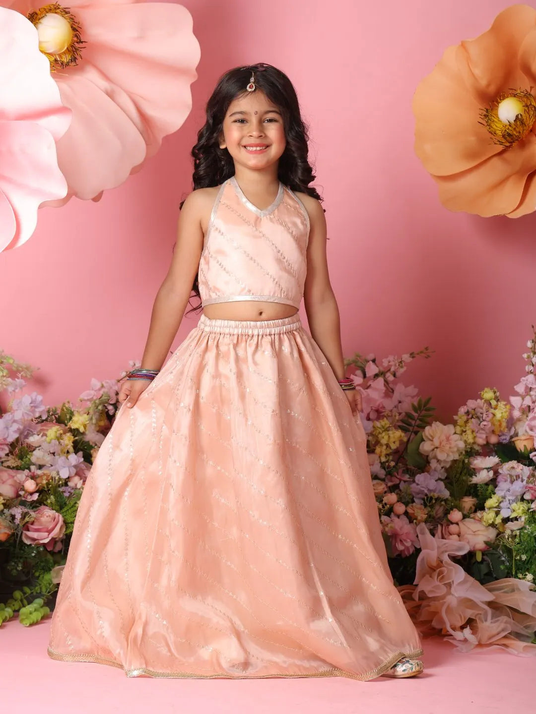 Young girl in a pink traditional outfit standing against a pink floral background