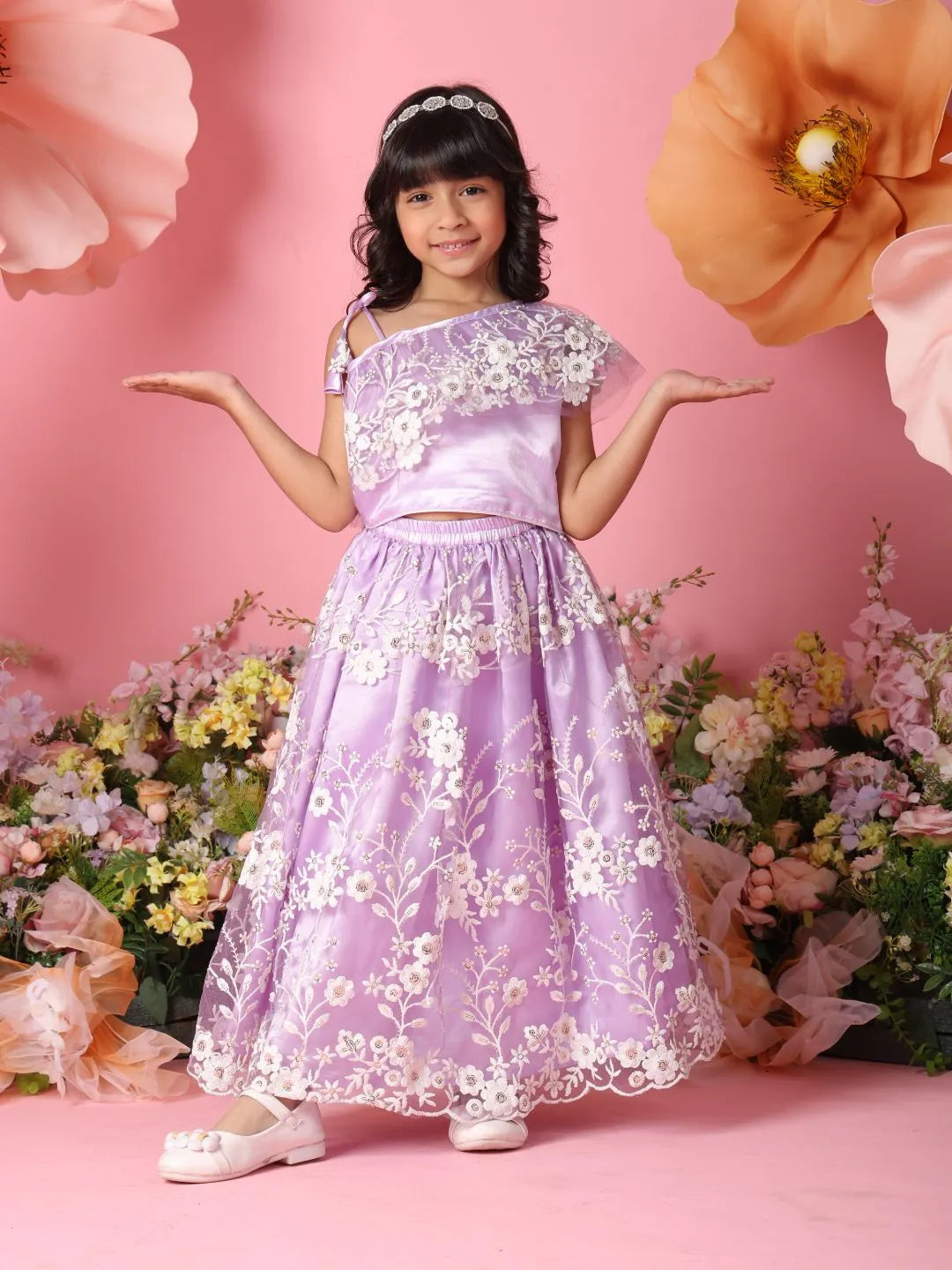 Young girl in a purple floral dress standing against a pink background with flowers.