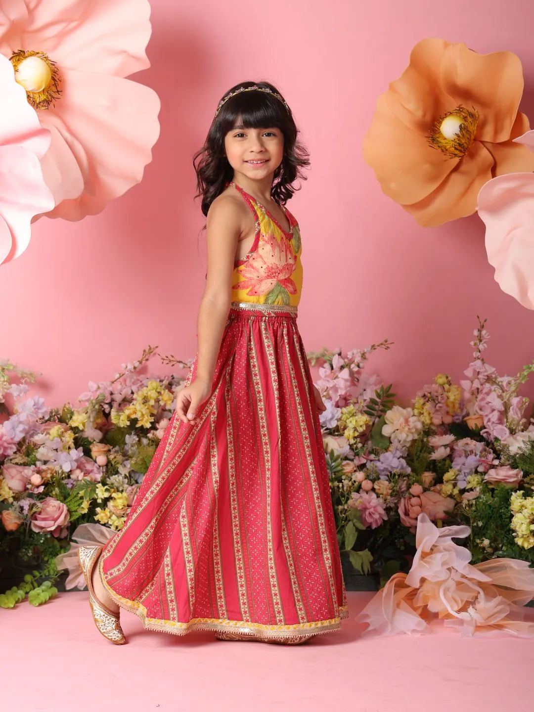 Young girl in a red and gold dress standing among flowers with a pink background