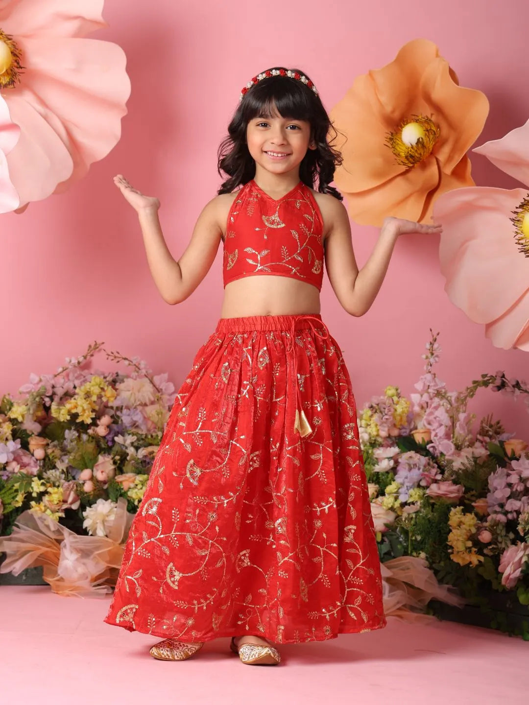 Young girl in a red floral dress standing against a pink background with flowers.
