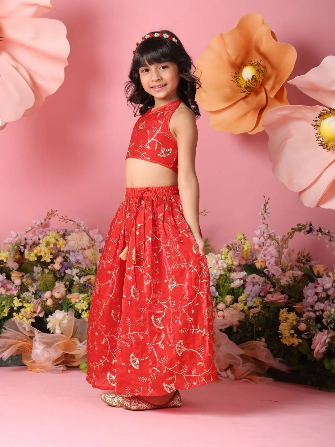 Young girl in a red floral dress standing in front of large flowers on a pink background