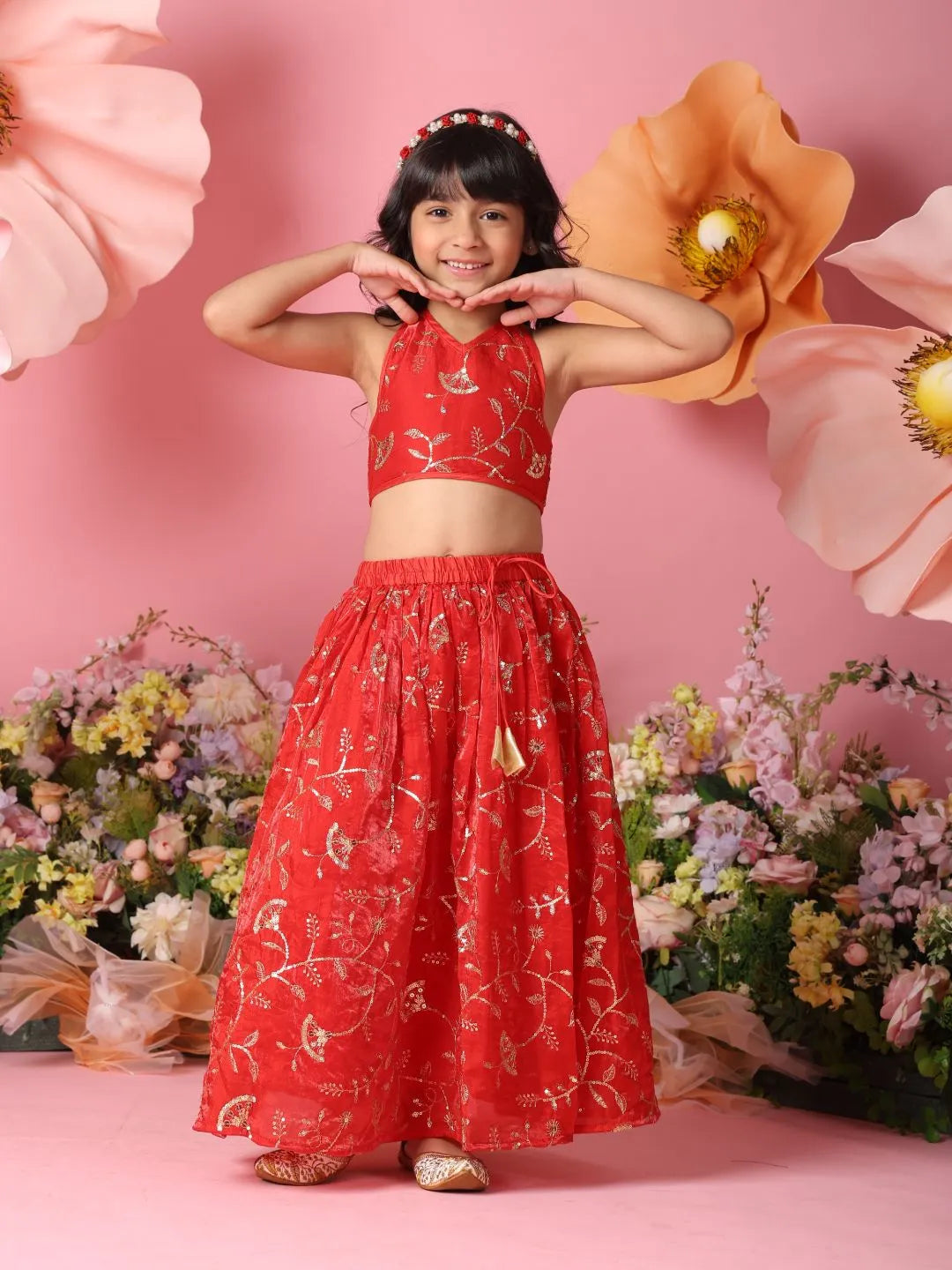 Young girl in a red floral outfit posing against a pink background with flowers.