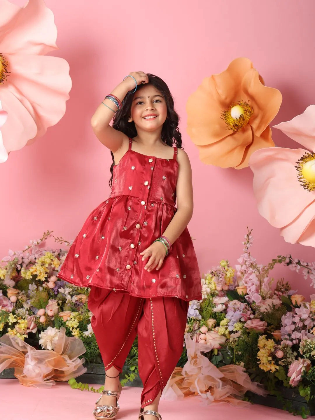 Young girl in a red outfit standing against a pink background with large flowers.