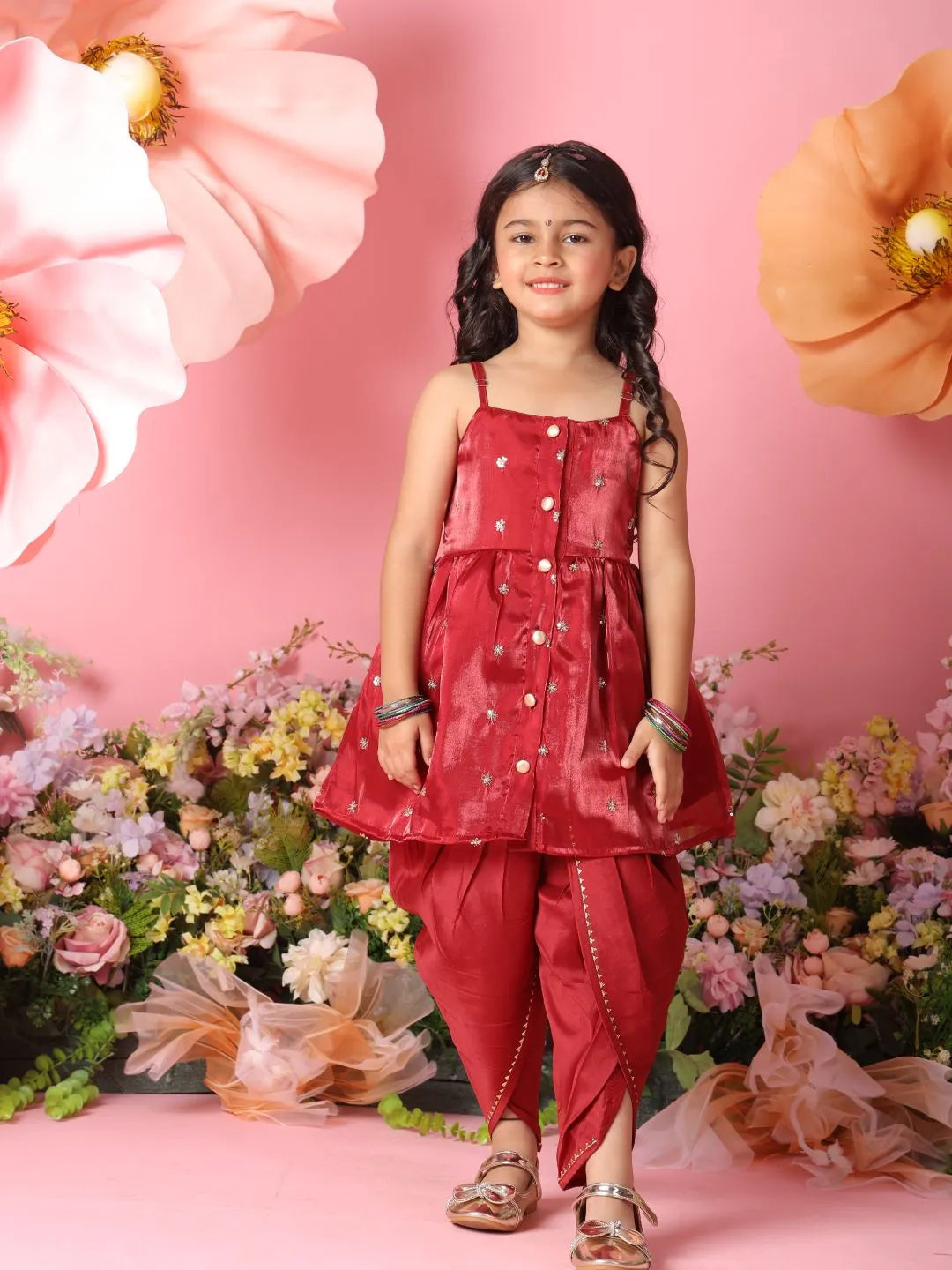 Young girl in a red traditional outfit standing against a pink floral background