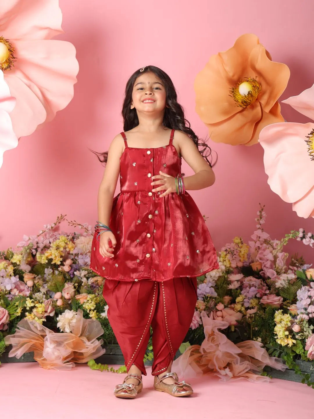 Young girl in a red traditional outfit standing against a pink floral background