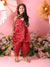 Young girl in a red traditional outfit standing in front of a floral backdrop with pink flowers.