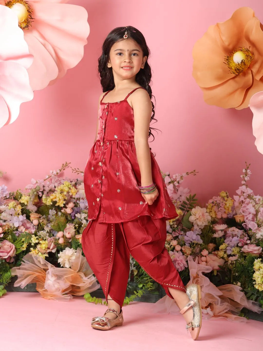Young girl in a red traditional outfit standing in front of flowers and decorative elements on a pink background