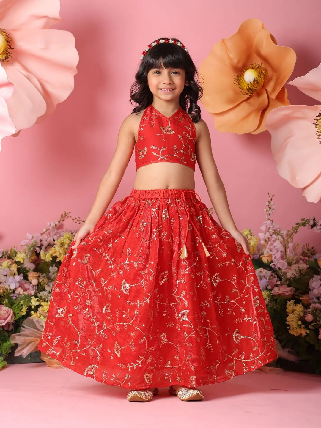 Young girl in a red traditional outfit with floral patterns against a pink background with flowers.