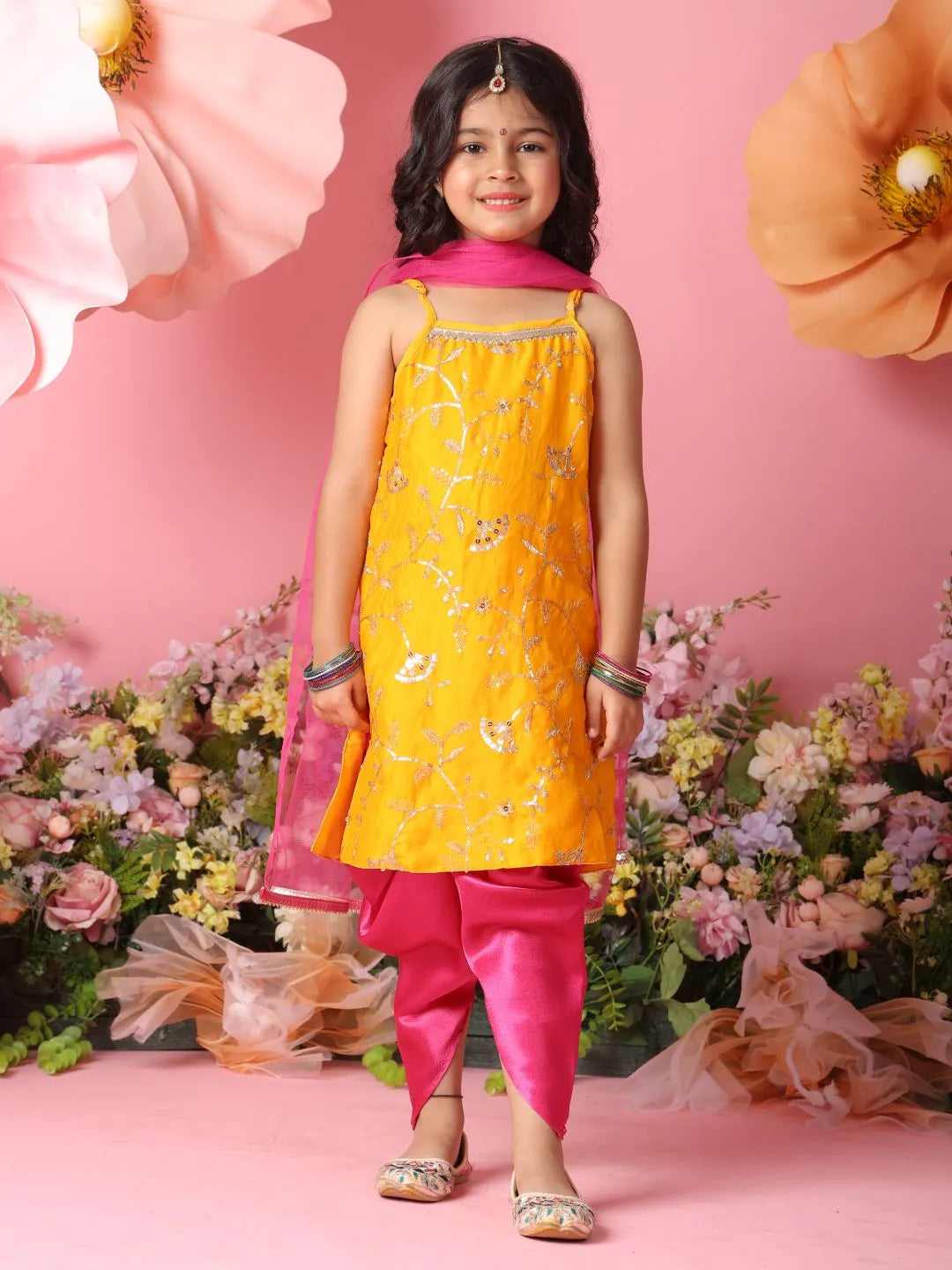 Young girl in yellow and pink traditional outfit with floral decorations and flowers in the background